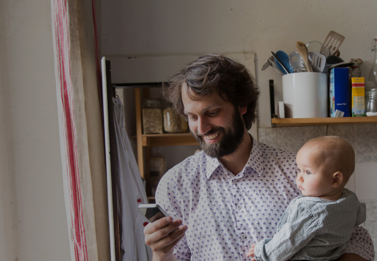 Smiling Dad Looking at Cellphone Holding Baby